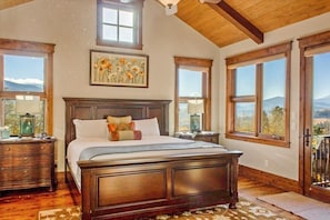 Ein Schlafzimmer mit einem großen Bett, einem Holzkopfende und mehreren Fenstern mit reizvollem Ausblick.