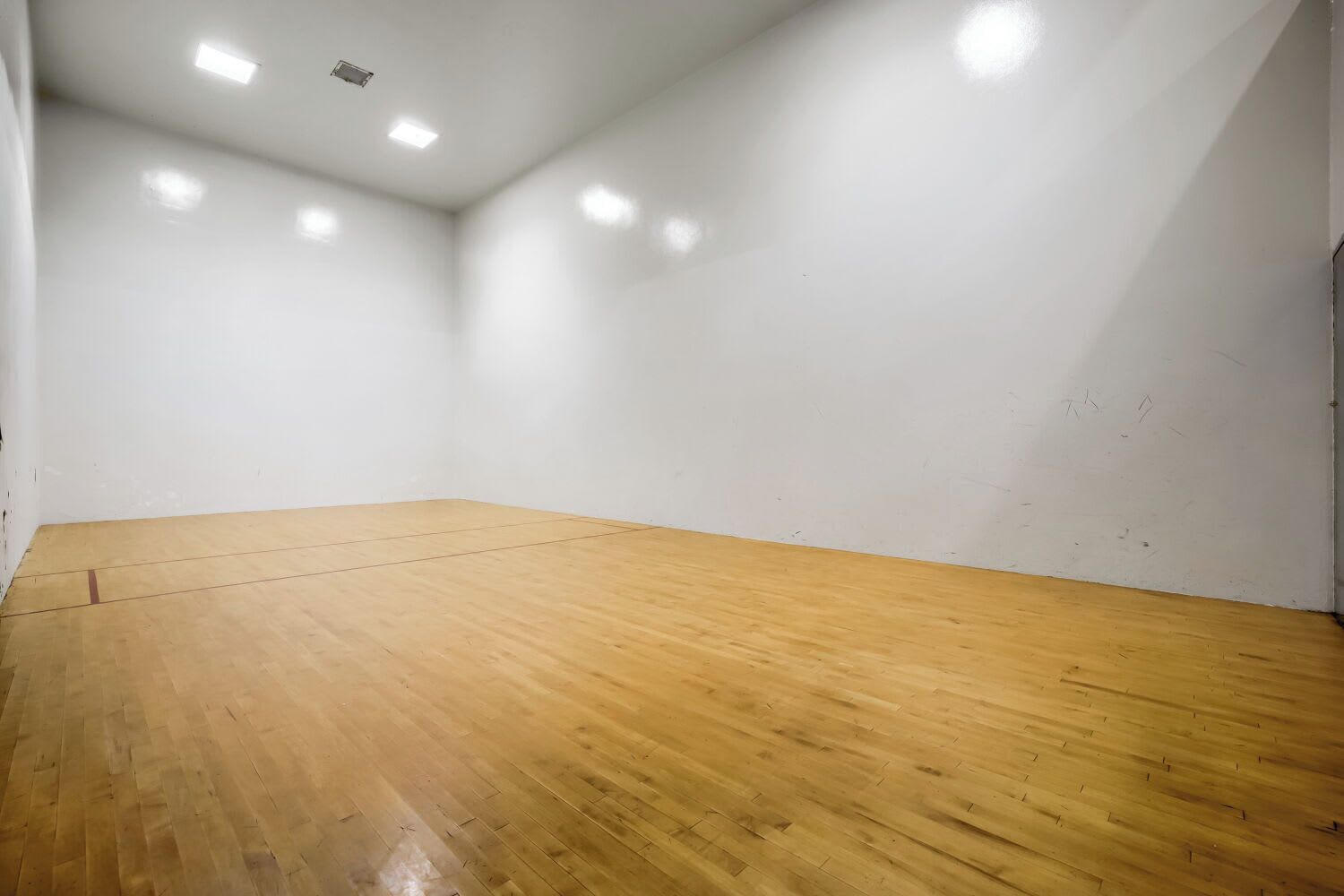 A room with a wooden floor, white walls, and recessed ceiling lights.