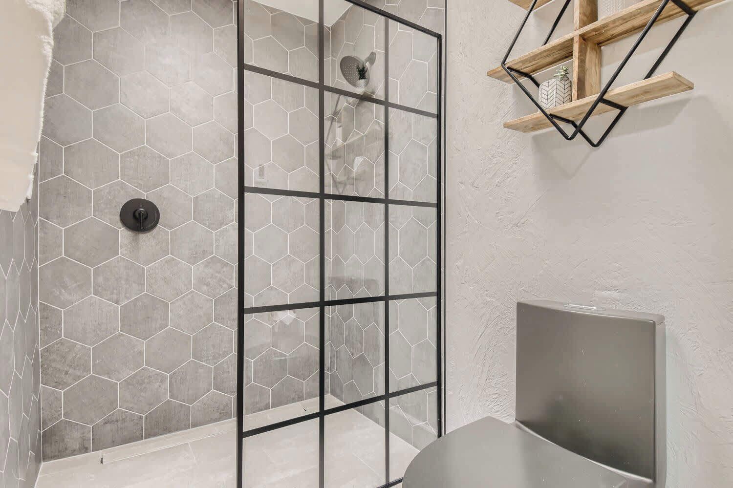 A shower with hexagonal tiles, a glass partition, and a wooden shelf with decorative items.