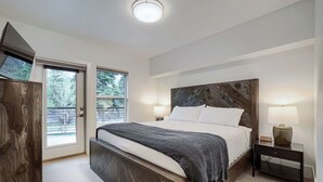 Ein Schlafzimmer mit einem großen Bett, einem Nachttisch mit Lampe, einem Holz-Kopfteil und einer Tür, die auf einen Balkon führt.