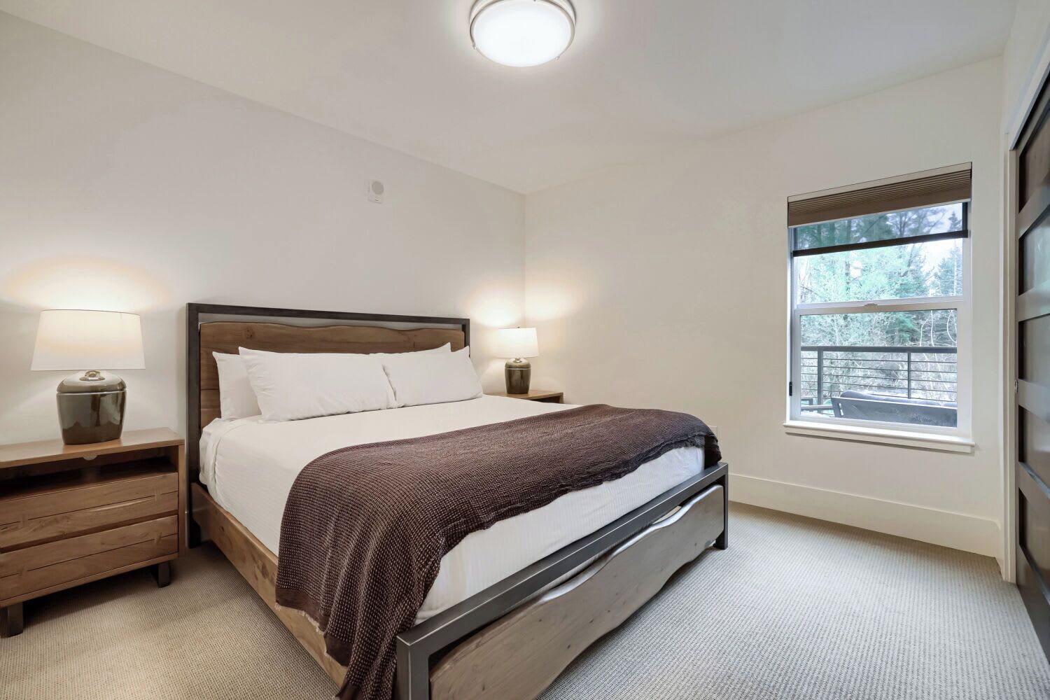 A bedroom with a bed, nightstands, a window, and a view of the outdoors.