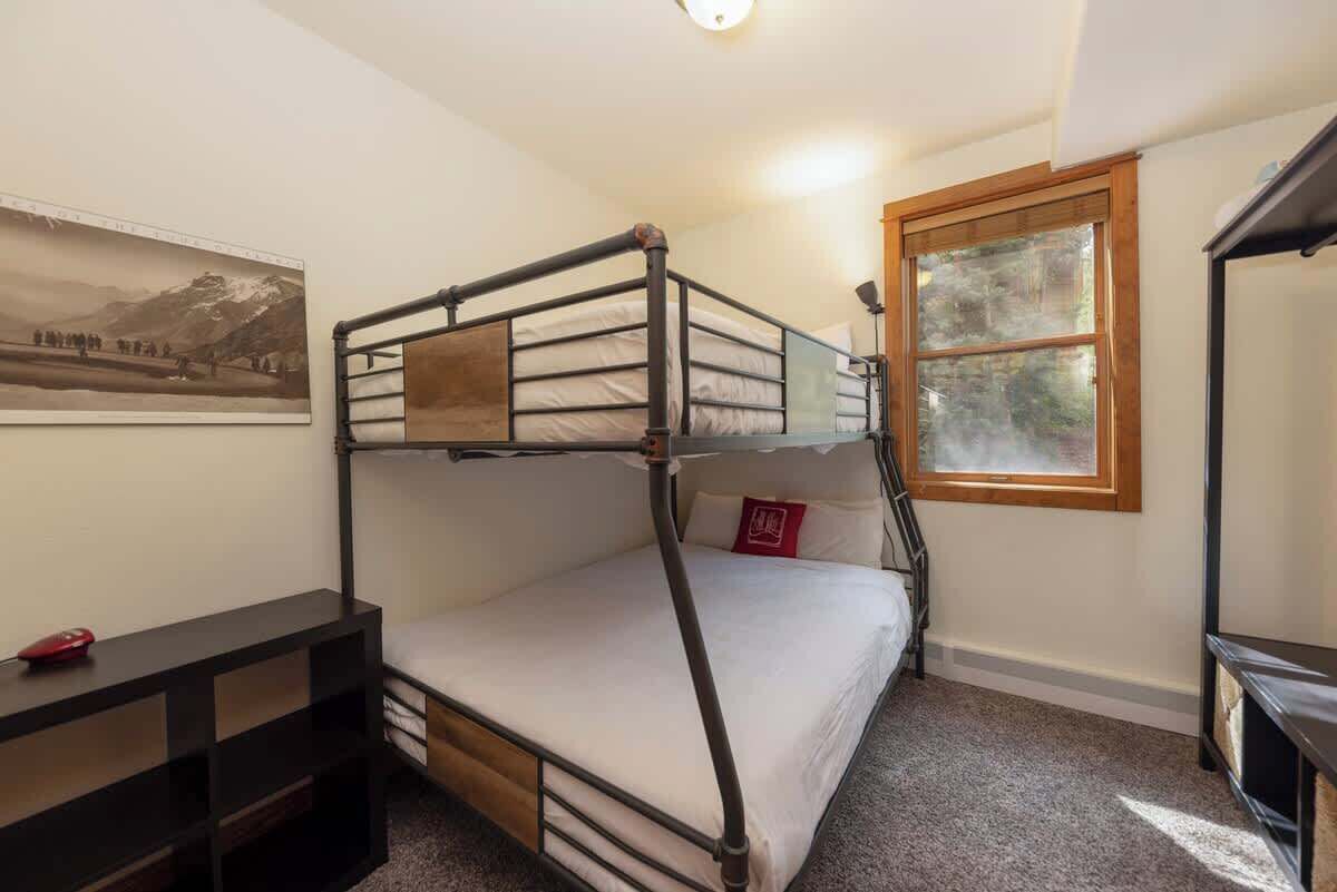 A bunk bed room with a desk, a window, and a framed picture on the wall.