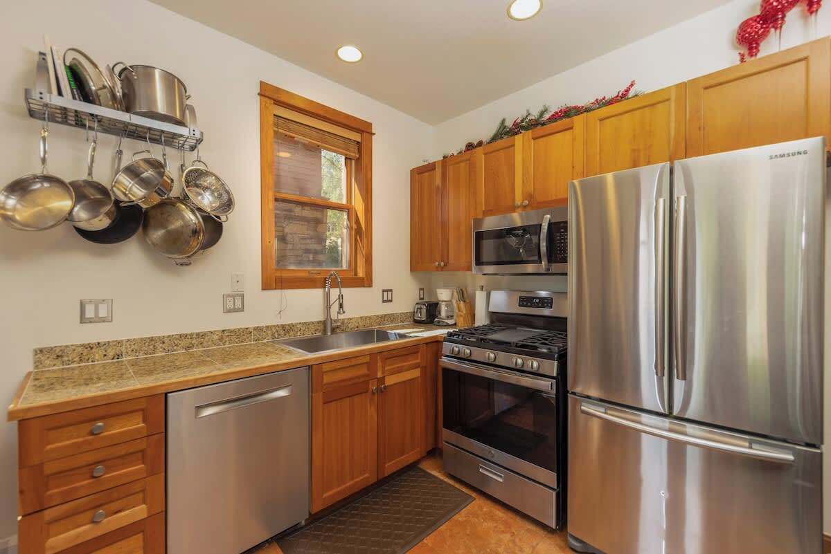 A kitchen with stainless steel appliances, wooden cabinets, a dish rack, and a window.