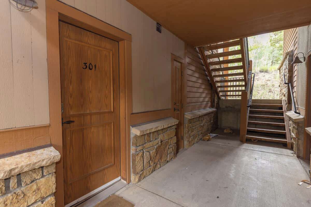 A wooden door with the number 301, a stone wall, a concrete floor, and a wooden staircase leading outside.