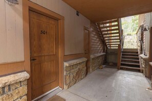 Eine Holztür mit der Nummer 301, eine Steinsäule, ein Betonboden und eine Holztreppe, die nach draußen führt.
