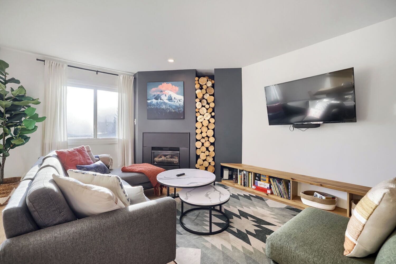 A modern living room with a sofa, a coffee table, a fireplace, a TV, and a bookshelf.