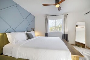 Ein Schlafzimmer mit Bett, Deckenventilator, Fenster mit Vorhängen und einem Spiegel.