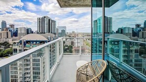 A balcony with a view of a cityscape, a wicker chair, and a glass railing. - Austin Rainey St. corner condo - lake views, private balcony, pool & gym (Austin)
