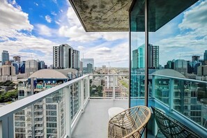 Ein Balkon mit Blick auf eine Stadtansicht, ein Korbstuhl und ein Glasgeländer.