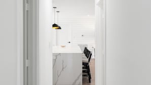 Et moderne køkken med en marmorø, hængende sort lysekrone og et spiseområde med en stol.