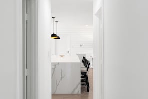 A modern kitchen with a marble island, black pendant lights, and a dining area with a chair. - Delila's Chic 3br 2ba with Heated Pool  (Deerfield Beach)