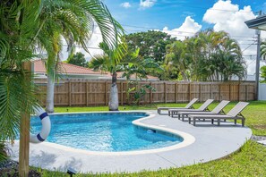 A swimming pool with a wooden fence, lounge chairs, and palm trees. - Delila's Chic 3br 2ba with Heated Pool  (Deerfield Beach)