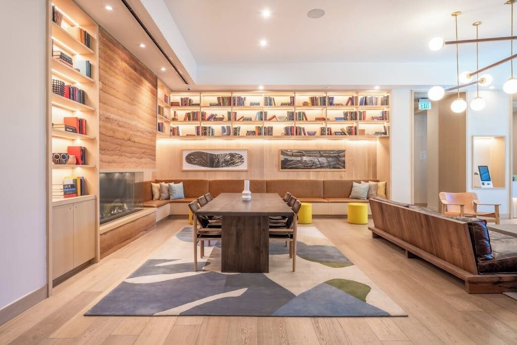 Une bibliothèque moderne dotée d’une grande table en bois au centre, d’étagères et d’espaces aménagés pour s’asseoir.