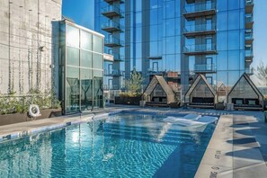 Um edifício moderno com piscina, fachada de vidro e áreas de estar ao ar livre.