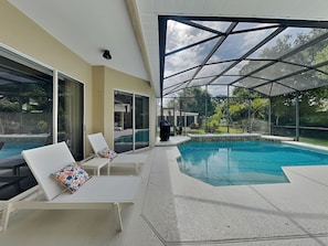 A covered outdoor swimming pool with lounge chairs and a patio area. - Sunrise Paradise (Port Orange)