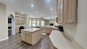 A spacious kitchen with wooden cabinets, a large island, and a dining area. - Sunrise Paradise (Port Orange)