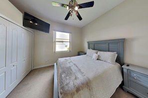 A bedroom with a bed, a ceiling fan, a TV, a window, and a nightstand. - Sunrise Paradise (Port Orange)