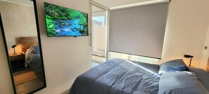 Ein Schlafzimmer mit einem Bett, einem an der Wand montierten Fernseher und einem Fenster mit Jalousie.