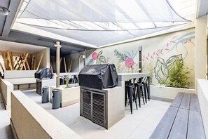 Eine Dachterrasse mit Grill, Sitzgelegenheiten und einem Wandgemälde.