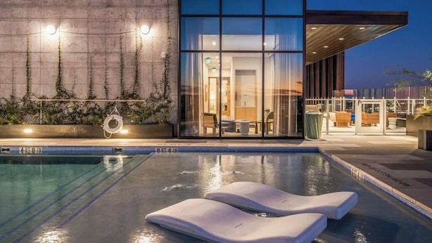 Ein modernes Gebäude mit Swimmingpool, Liegestühlen und einer Glasfassade.