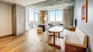 Ein geräumiges Zimmer mit großem Fenster, einem runden Tisch, einer Couch und einem Fernseher.