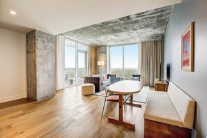 Ein geräumiges Zimmer mit großem Fenster, einem runden Tisch, einer Couch und einem Fernseher.