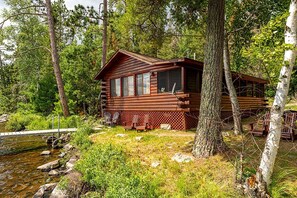 Eine Blockhütte mit einer Terrasse, umgeben von Bäumen und einem kleinen Bach.