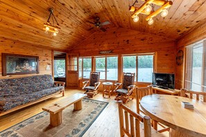 L’intérieur d’un chalet en bois, avec un canapé, des fauteuils, un téléviseur et une cheminée.