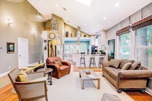 A spacious living area with a sofa, armchair, and coffee table, a kitchen with bar stools, and large windows. - Quiet central home with enclosed yard, deck, grill, central AC, & washer/dryer (Austin)