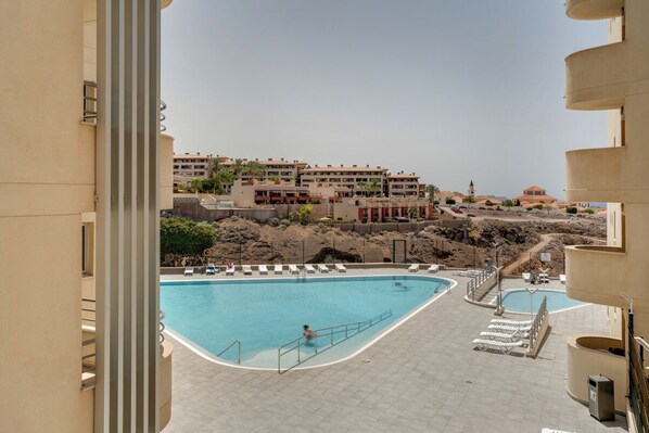 Ein Poolbereich mit mehreren Schwimmbecken, Liegestühlen und Blick auf die umliegenden Gebäude.