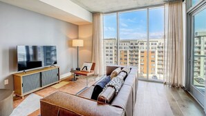 Un salon moderne avec une grande télévision, un canapé et une vue sur des immeubles de grande hauteur.