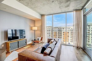 Ein modernes Wohnzimmer mit großem Fernseher, einer Couch und Blick auf hohe Gebäude.