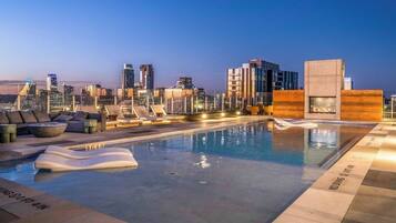 A rooftop pool with a city skyline view, lounge chairs, and a modern poolside area.