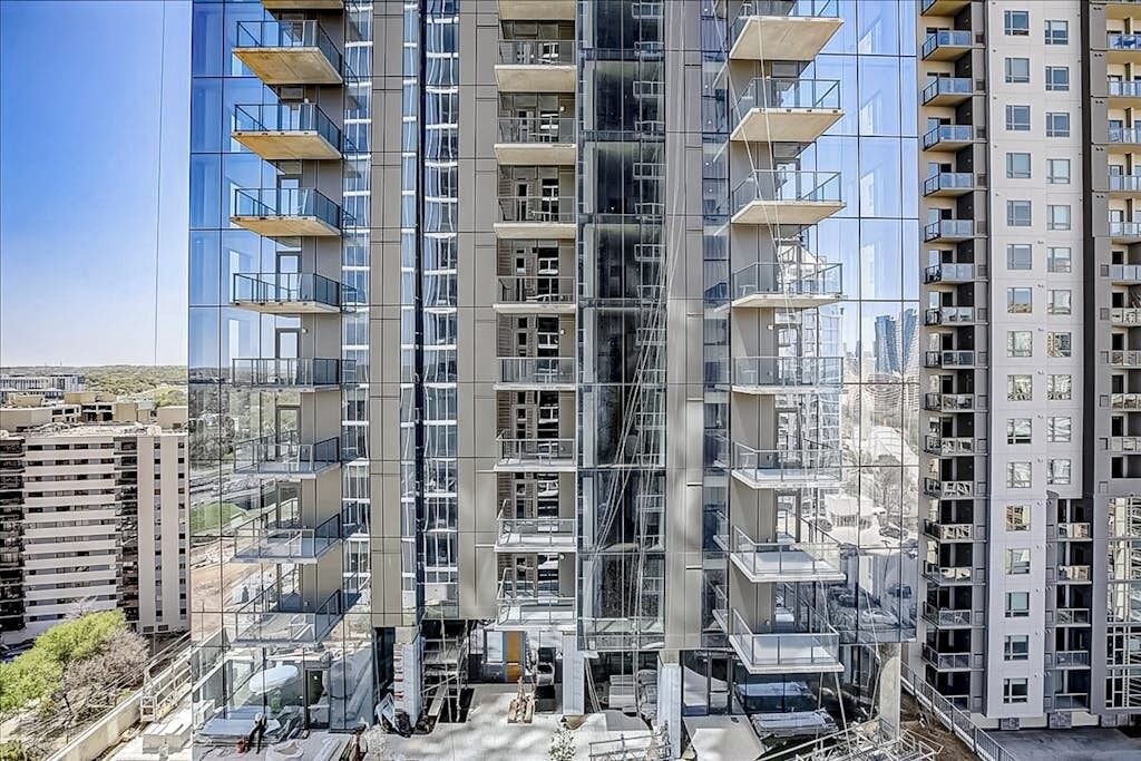A modern high-rise building with multiple balconies, large windows, and a clear view of the surrounding area.