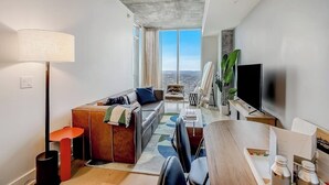 Una sala de estar moderna con un sofá, una mesa de centro, televisor y un ventanal con vistas a la ciudad.