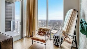 Una habitación moderna con un ventanal grande, una butaca acolchada, una mesita y un espejo.