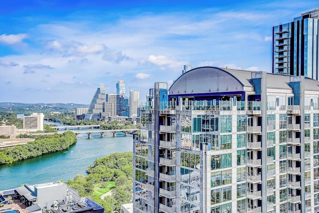 A modern high-rise building with a glass facade, a dome structure on the top, and a river in the background.