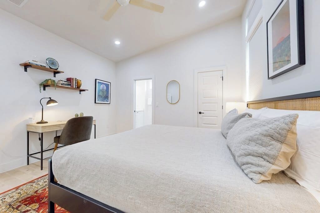 Une chambre à coucher comprenant un lit, un bureau, des étagères, une chaise et un ventilateur de plafond.
