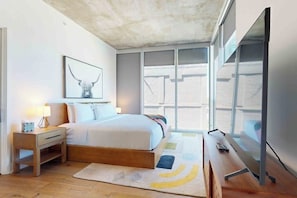 Ein Schlafzimmer mit Bett, Nachttisch, Lampe und einem großen Fenster.
