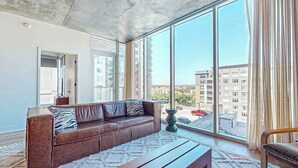 Uma sala de estar moderna com um sofá de couro, um banco de madeira e grandes janelas com vista para a cidade.