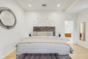 Un dormitorio con cama, mesitas de noche, un espejo y una pared con detalles decorativos.