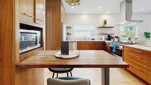 A modern kitchen with wooden cabinets, a central island, a microwave, and a hanging light fixture. - Stunning dog-friendly house w/private gas grill & deck -steps to South Congress (Austin)