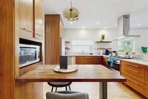 A modern kitchen with wooden cabinets, a central island, a microwave, and a hanging light fixture. - Stunning dog-friendly house w/private gas grill & deck -steps to South Congress (Austin)