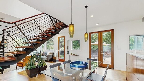 A modern interior with a glass dining table, a staircase with a metal railing, and a view through large windows. - Stunning dog-friendly house w/private gas grill & deck -steps to South Congress (Austin)