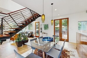 Een modern interieur met een glazen eettafel, een trap met metalen leuning en een uitzicht door grote ramen.