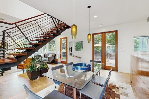 A modern interior with a glass dining table, a staircase with a metal railing, and a view through large windows. - Stunning dog-friendly house w/private gas grill & deck -steps to South Congress (Austin)
