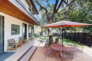 Un patio con mobiliario exterior, una mesa redonda y un paraguas rojo.