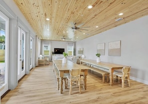 Una habitación amplia con techo de madera, una larga mesa de comedor con sillas, un sofá y un televisor.