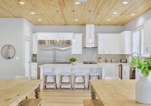 Una cocina moderna con armarios blancos, una isla central con taburetes e iluminación colgante.