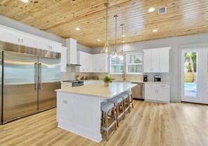 A modern kitchen with wooden ceiling, stainless steel appliances, white cabinetry, and a central island with bar stools. - Poseidon’s Palace | 11BR | Steps 2 Beach | Heated Pool/Spa | Sleeps 28 | Games (Destin)